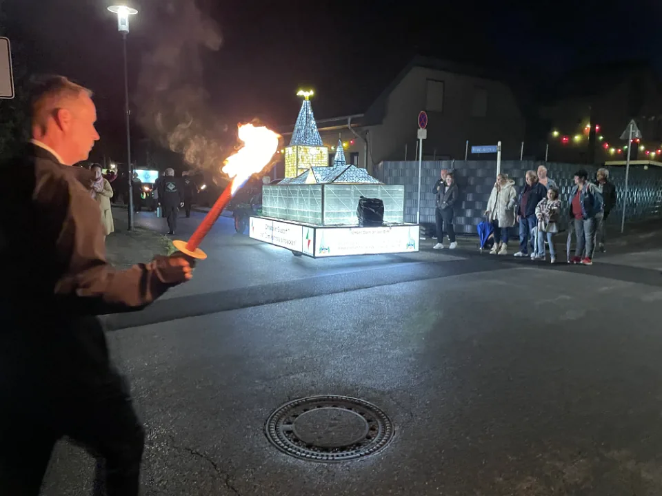 Ein beleuchtetes Fackelmotiv und Fackelträger ziehen bei Nacht durch Gustorf.