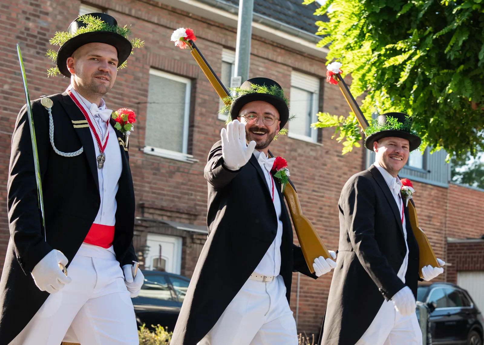 Drei Schützen mit dunklen Jacken, Hüten und weißen Hosen im Festzug.