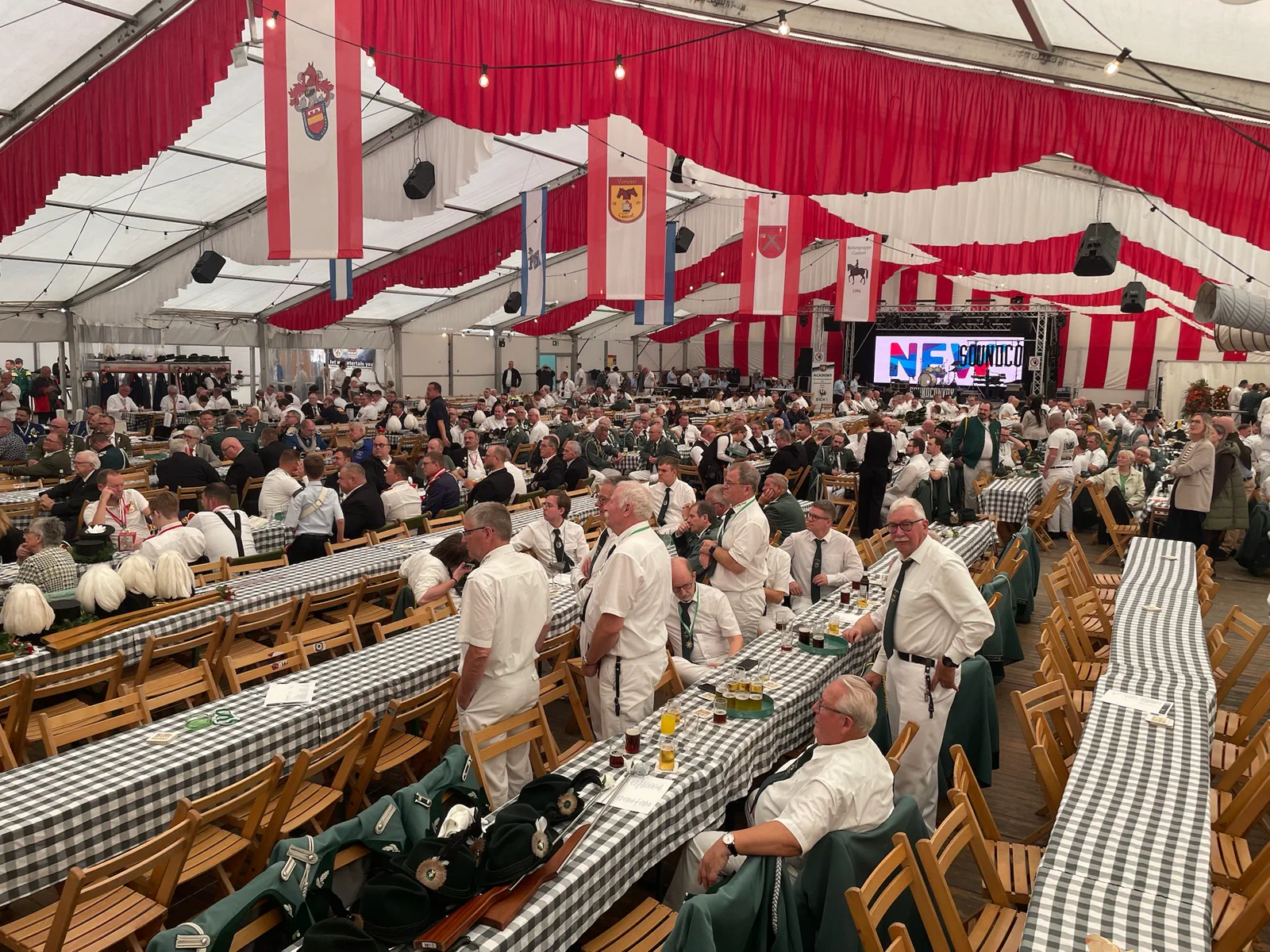 Besucher sitzen an langen Tischen unter rot-weißen Girlanden im Festzelt.